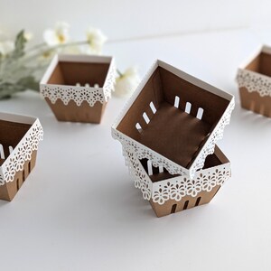 Five lace-edge paper berry baskets made from kraft cardstock with white floral lace rims, arranged on a white background with soft spring flowers, shown as a Lace Berry Basket SVG treat holder and favor box template for Cricut and cutting machines.