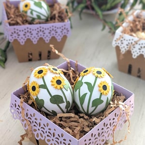 Lavender lace-edge paper berry basket in kraft cardstock filled with shredded paper and sunflower-decorated Easter eggs, styled on a light wood surface with additional baskets in the background for a Lace Easter Basket SVG treat holder template for Cricut and cutting machines.