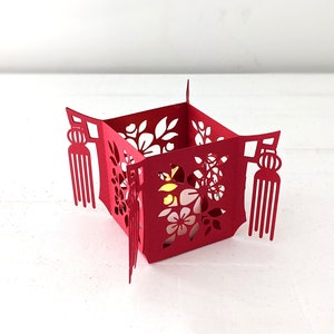 Red paper Chinese tea light holder with floral cutouts and tassel accents, made from a 3D SVG template and illuminated with a small LED light.