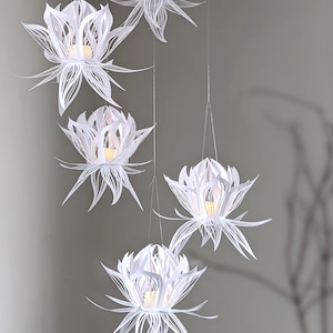 Set of five white 3D paper lotus lanterns hanging from the ceiling, each lit with a flickering LED light, made using a lotus lantern SVG for Cricut and Silhouette.