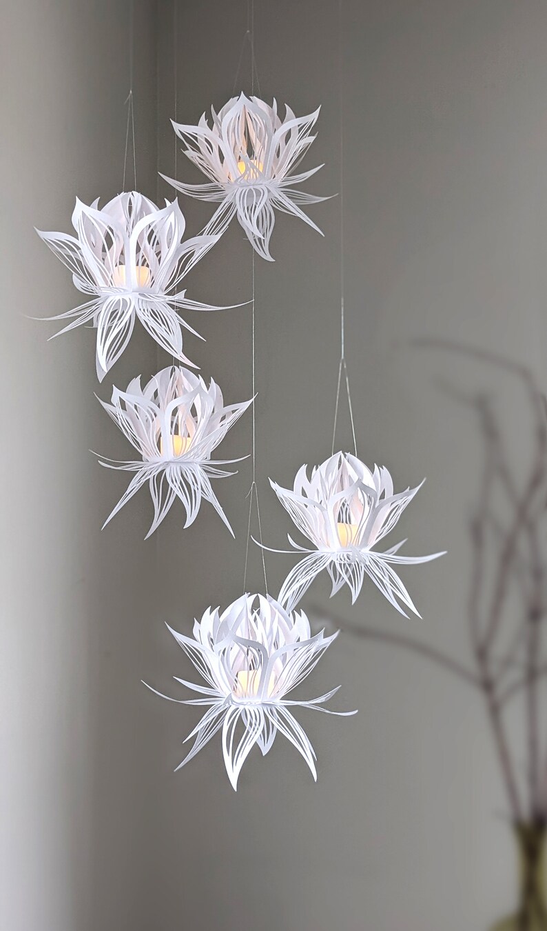 Set of five white 3D paper lotus lanterns hanging from the ceiling, each lit with a flickering LED light, made using a lotus lantern SVG for Cricut and Silhouette.