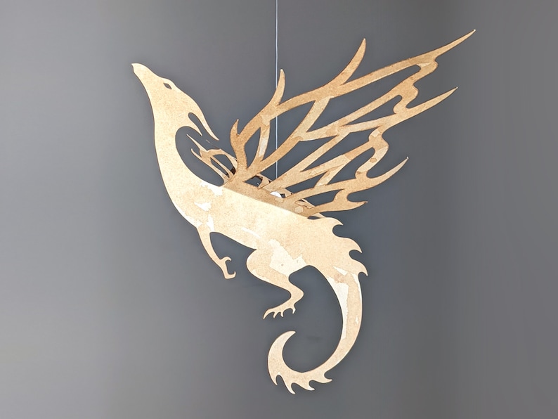 May include: A beige paper dragon mobile with intricate cut-out wings and a curled tail. The dragon is suspended from a string.