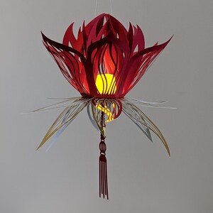Red 3D paper lotus lantern with gold leaf accents and a hanging tassel, illuminated by an LED tealight inside, created using a lotus lantern SVG for Cricut and Silhouette.
