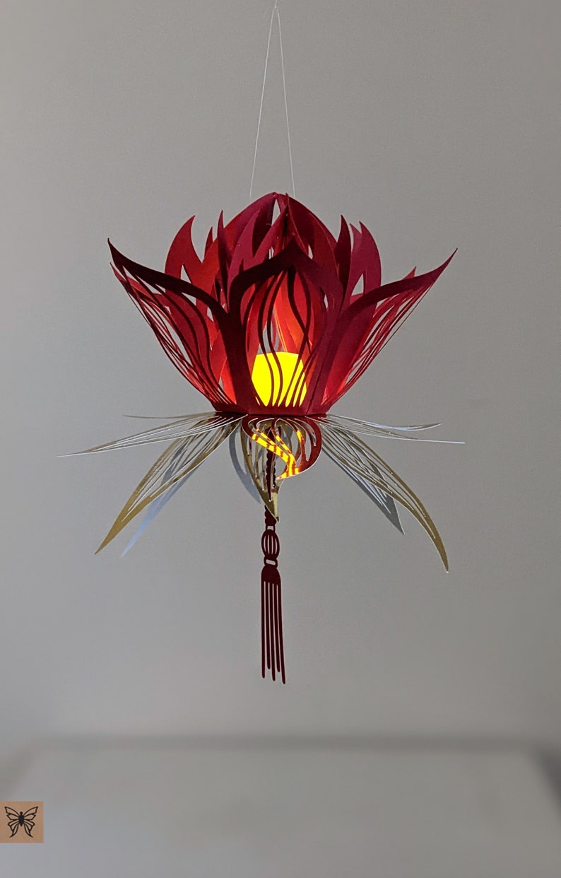 Red 3D paper lotus lantern with gold leaf accents and a hanging tassel, illuminated by an LED tealight inside, created using a lotus lantern SVG for Cricut and Silhouette.