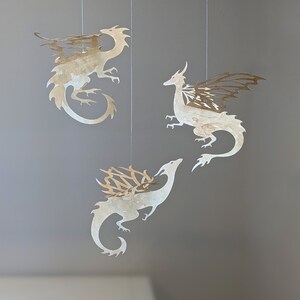 May include: Three paper cut-out dragons hanging from the ceiling. The dragons are white with gold accents and have intricate wing designs.
