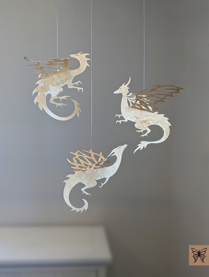 May include: Three paper cut-out dragons hanging from the ceiling. The dragons are white with gold accents and have intricate wing designs.