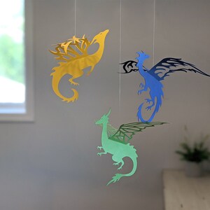 May include: Three paper dragon mobiles hanging from the ceiling. The dragons are yellow, blue, and green.
