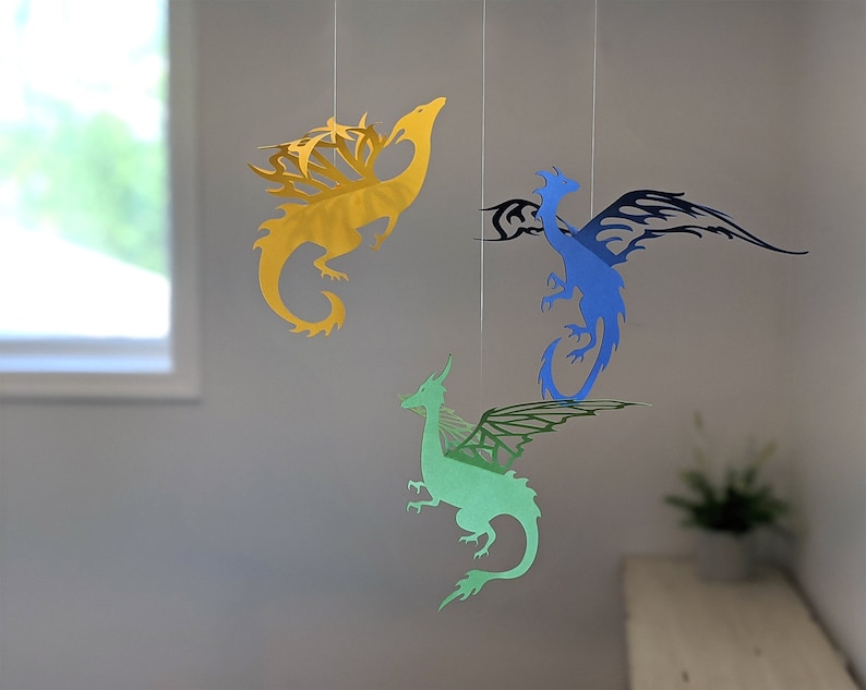 May include: Three paper dragon mobiles hanging from the ceiling. The dragons are yellow, blue, and green.
