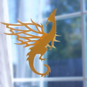 Hanging paper dragon mobile in golden cardstock, Caspian dragon SVG design displayed in front of a window for fantasy room decor