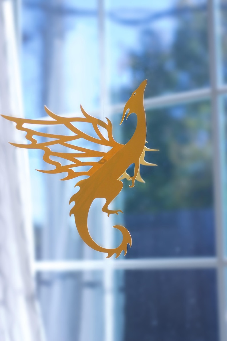 Hanging paper dragon mobile in golden cardstock, Caspian dragon SVG design displayed in front of a window for fantasy room decor