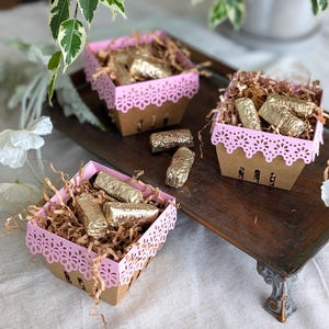 Pink Lace Berry Basket paper treat boxes filled with chocolates and paper filler, displayed on a decorative tray with flowers and greenery. A charming DIY party favor idea for birthdays, showers, weddings, and special celebrations.