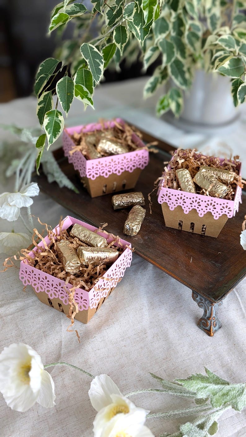 Pink Lace Berry Basket paper treat boxes filled with chocolates and paper filler, displayed on a decorative tray with flowers and greenery. A charming DIY party favor idea for birthdays, showers, weddings, and special celebrations.