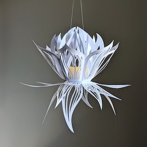 Single white 3D paper lotus lantern hanging from a string with a flickering LED tealight inside, crafted using a lotus lantern SVG for Cricut and Silhouette.