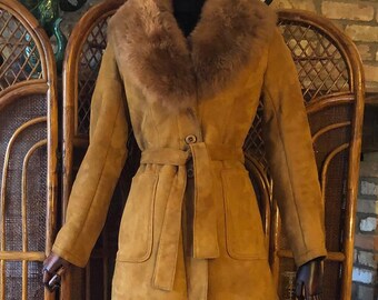 May include: A brown suede jacket with a faux fur collar and a tie belt. The jacket is on a mannequin wearing a floral skirt.