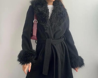 May include: A black coat with a faux fur collar and cuffs. The coat has a tie belt at the waist and a long, flowing design. The coat is a classic style, suitable for various occasions.