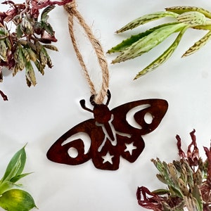 May include: A rustic brown metal butterfly ornament with a twine hanger. The butterfly has a cutout design of moons and stars.