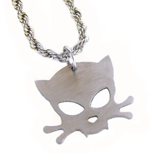 May include: Silver-toned pendant necklace featuring a cat-shaped design. The pendant is attached to a silver rope chain. The cat silhouette has cut-out eyes and a mouth, and the design includes two stylized whiskers.