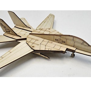 May include: A wooden model of a fighter jet, featuring detailed wing and tail designs. The model has a natural wood finish with visible grain and includes markings such as a star and a circular emblem. The wingspan is approximately 10 inches.
