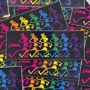 May include: Rectangular black sticker featuring a line of dancing skeletons in rainbow colors, each wearing a top hat. The text "J.Rows" is in the lower left corner. The skeletons are in various poses, with arms raised and legs kicking.