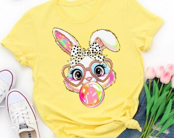 May include: A yellow t-shirt with a cartoon bunny wearing heart-shaped glasses and blowing a bubblegum bubble. The bubblegum is decorated with colorful Easter egg designs.