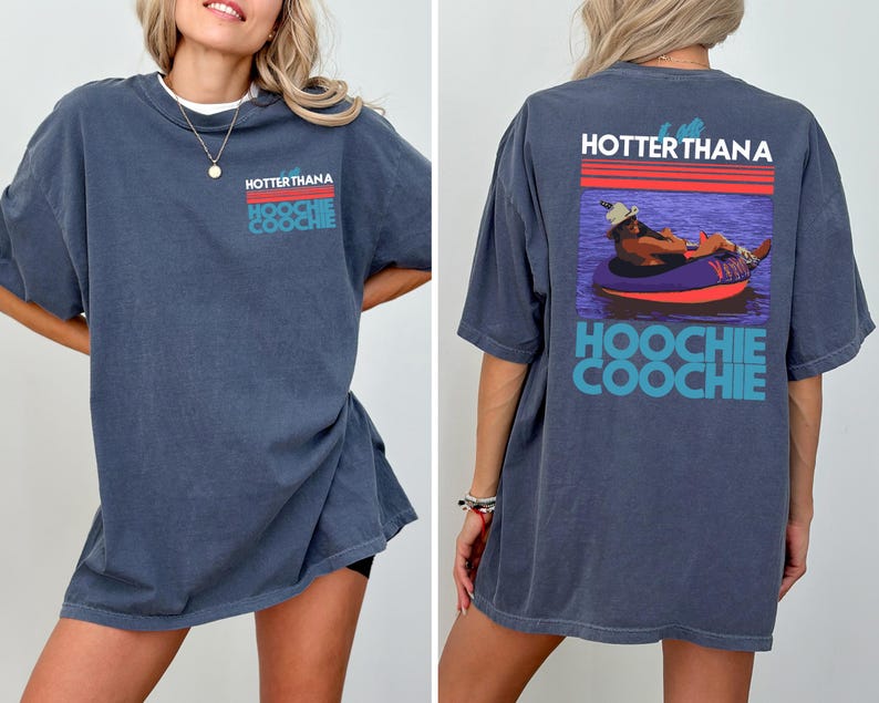 May include: A dark blue t-shirt featuring a graphic on the front left chest and a larger version on the back. The design includes red and teal stripes with the text "HOTTER THAN A HOOCHIE COOCHIE" and an illustration of a person in a tube.