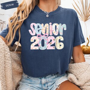 May include: Navy blue t-shirt featuring the word "Senior" and the year "2026" in a colourful floral and patterned design. The word "Denim" is printed on a navy blue banner in the upper left corner.