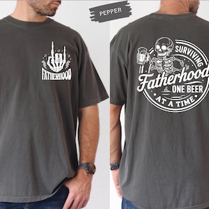 Pu&ograve; includere: T-shirt color pepe con grafiche bianche. La parte anteriore presenta un gesto della mano scheletrica e la parola "FATHERHOOD". Il retro mostra uno scheletro che tiene una birra, con il testo "SURVIVING FATHERHOOD ONE BEER AT A TIME".