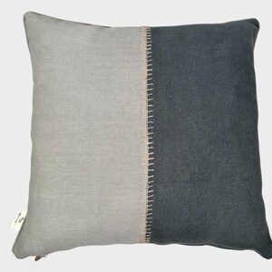 May include: A grey and dark grey decorative cushion with a contrasting beige seam down the centre.