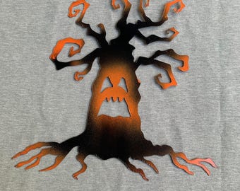 Può includere: Silhouette di albero in metallo a tema Halloween con una faccia di jack-o'-lantern intagliata nel tronco. L'albero è nero con riflessi arancioni sui rami e sulle radici, su sfondo grigio.