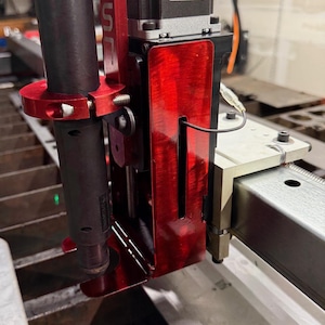 May include: Close-up of a red and black metal cutting machine. The machine has a red housing with the letters "SR" on it. A black cylindrical component is attached to the red housing. A label on the machine reads "LANGMUIR SYSTEMS".