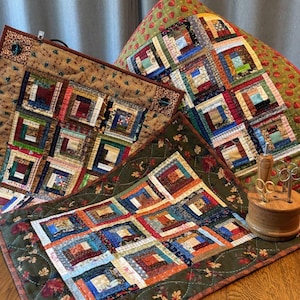 May include: A collection of handmade quilts with a patchwork design. The quilts feature squares of various colors and patterns, including red, blue, green, and brown. A wooden spool with scissors is also visible.