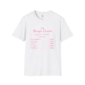 Può includere: T-shirt bianco con la scritta rosa "THE Bougie Cousin". Sotto, un'etichetta nutrizionale indica: High Standards 100%, First Class 100%, Extra 100%, Self Love 100% e Never Basic 100%.