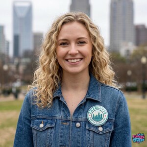 Pu&ograve; includere: Una donna indossa una giacca di jeans blu con una toppa circolare che recita "Charlotte North Carolina" con una grafica dello skyline. La donna ha i capelli biondi ricci e sorride. Lo sfondo presenta uno skyline cittadino e spazi verdi.