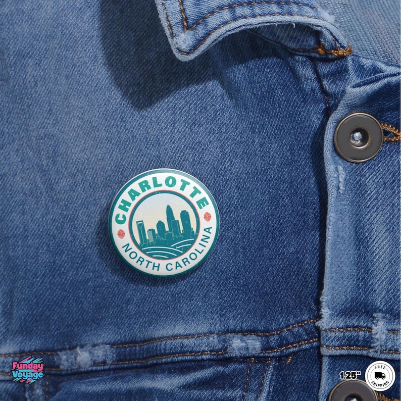 Pu&ograve; includere: Una spilla rotonda con un design turchese e bianco raffigurante lo skyline di Charlotte, Carolina del Nord. La spilla &egrave; attaccata a una giacca di jeans. Il testo "CHARLOTTE NORTH CAROLINA" &egrave; stampato attorno al bordo della spilla.