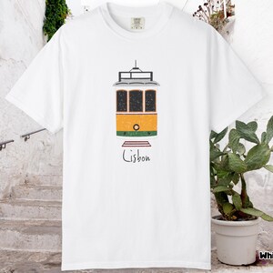 K&ouml;nnte beinhalten: Wei&szlig;es T-Shirt mit einer Illustration einer gelb, orange und gr&uuml;n gef&auml;rbten Stra&szlig;enbahn aus Lissabon. Unter der Stra&szlig;enbahn steht in handschriftlicher Schrift das Wort "Lisbon".