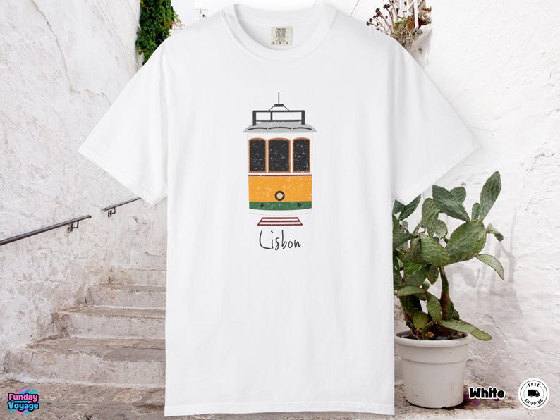 K&ouml;nnte beinhalten: Wei&szlig;es T-Shirt mit einer Illustration einer gelb, orange und gr&uuml;n gef&auml;rbten Stra&szlig;enbahn aus Lissabon. Unter der Stra&szlig;enbahn steht in handschriftlicher Schrift das Wort "Lisbon".