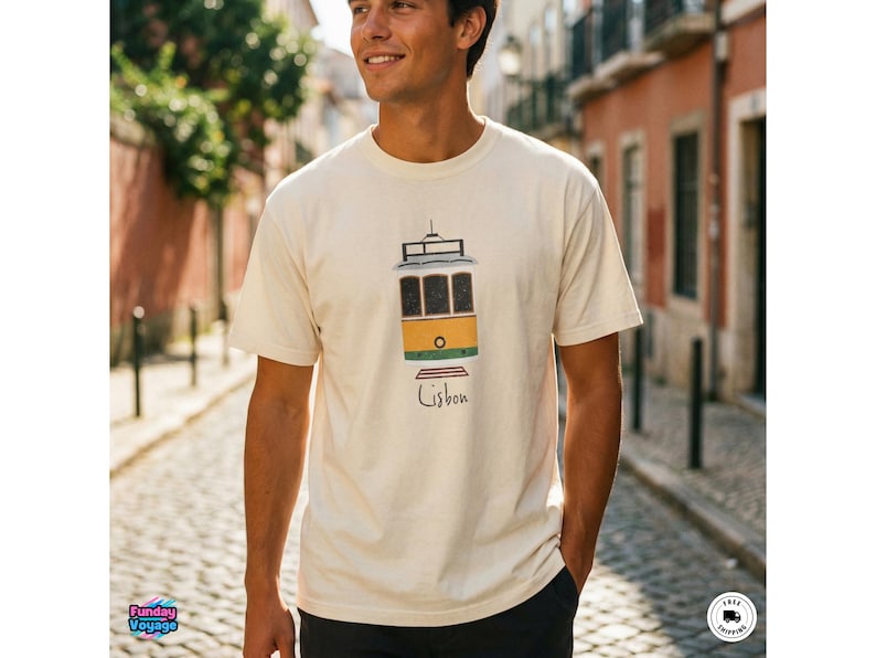 K&ouml;nnte beinhalten: Cremefarbenes T-Shirt mit einer farbenfrohen Illustration einer Lissabonner Stra&szlig;enbahn. Die Stra&szlig;enbahn ist gelb, gr&uuml;n und braun, mit dem Wort "Lissabon" darunter. Das Shirt ist aus weichem Material und f&uuml;r den Freizeitgebrauch geeignet.