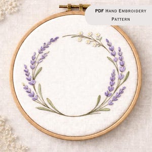 May include: A hand embroidery pattern in a wooden hoop. The design features a lavender wreath with purple flowers and green leaves. The text "PDF Hand Embroidery Pattern" is displayed in the upper right corner.