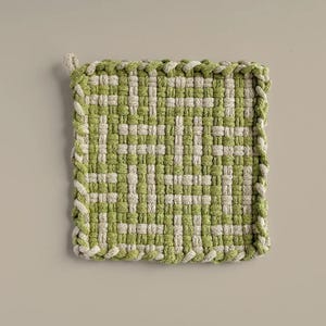 May include: A green and white woven pot holder with a fringed edge.