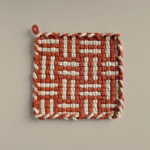 May include: A woven pot holder with a geometric pattern in orange and white. The pot holder is square and has a fringe border.