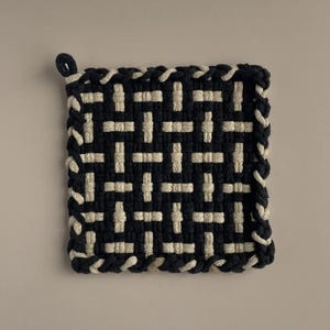 Könnte beinhalten: Schwarzer und weißer gewebter Topflappen mit geflochtenem Rand.