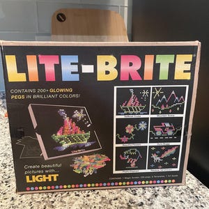 May include: A Lite-Brite box with the product name in colorful letters. The box features a sample image of a boat made with colorful pegs. The box states it contains 200+ glowing pegs and includes templates.
