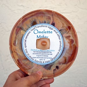 May include: A ceramic dish with a brown and orange glaze. The dish has a round, indented center and is labeled "Omelette Maker". The label also includes instructions for making an omelette in the dish.