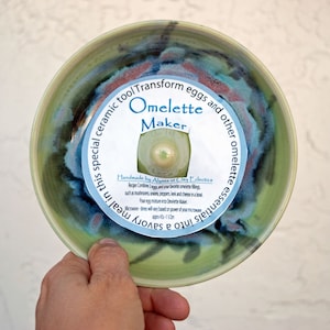 May include: A green ceramic bowl with blue and pink accents. The bowl has a white label that says "Omelette Maker" and includes instructions for making omelettes in the microwave. The label also says "Handmade by Alyssa at Clay Eclectics".
