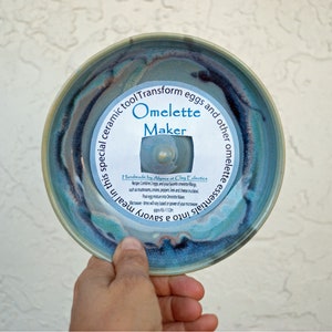 Puede incluir: Un molde para tortilla de cerámica azul y verde con el texto "Transform eggs and other omelette essentials into a savory meal in this special ceramic tool Omelette Maker" y "Handmade by Alyssa at Clay Eclectics".