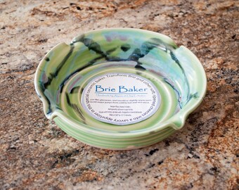 May include: Green ceramic brie baker with a white label that reads "Brie Baker Handmade by Alana of Clay Creations" and instructions for using the baker.  The baker is on a speckled countertop.