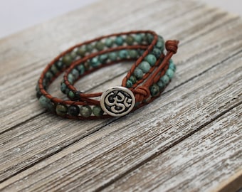 May include: A brown leather wrap bracelet with turquoise beads and a silver Om charm.