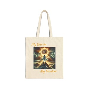 Può includere: Una borsa tote beige con il testo "My Bitcoin" e "My Freedom" stampato in arancione. La borsa presenta una grafica di una persona che tiene una grande moneta d'oro Bitcoin.