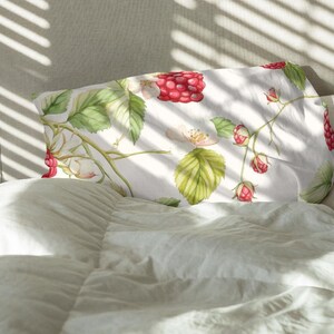 May include: White pillowcase with a watercolor design of raspberries, green leaves, and white flowers. The pillowcase is rectangular and rests on a white bed. The design features red raspberries and green leaves.