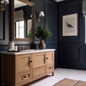 Puede incluir: Un tocador de ba&ntilde;o de madera clara con tres cajones y dos gabinetes. El tocador tiene herrajes negros y una encimera blanca. El tocador est&aacute; en un ba&ntilde;o azul oscuro con una impresi&oacute;n enmarcada de un p&aacute;jaro y un espejo sobre el tocador.